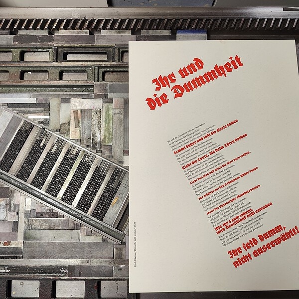 Foto des Druckbogens mit der fertig gesetzten roten und schwarzen Druckform. Es ist ein Gedicht von Kästner von 1932, "Ihr und die Dummheit"
