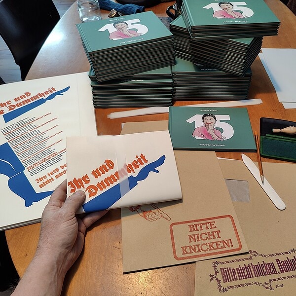 Foto der Packtischsituation in der Wohnküche beim einschlagen des Sammelbandes No. 15 in das vorbereitete Einbandposter mit dem Gedicht Erich Kästners.