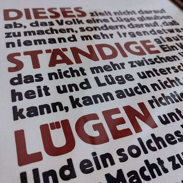 Foto Detail des fertig gerahmten Druckes in Bordaux Rot und Schwarz Blau eines Textes von Hannah Arendt. Der Text lautet: Dieses ständige Lügen zielt nicht darauf ab, das Volk eine Lüge glauben zu machen, sondern darauf, dass niemand mehr irgendetwas glaubt. Ein Volk, das nicht mehr zwischen Wahrheit und Lüge unterscheiden kann, kann auch nicht zwischen richtig und falsch unterscheiden. Und ein solches Volk, das sich seiner Macht, zu denken und zu urteilen, beraubt sieht, ist auch, ohne zu wissen und zu wollen, dem Gesetz der Lüge vollständig unterworfen. Mit einem solchen Volk kann man dann machen, was man will.