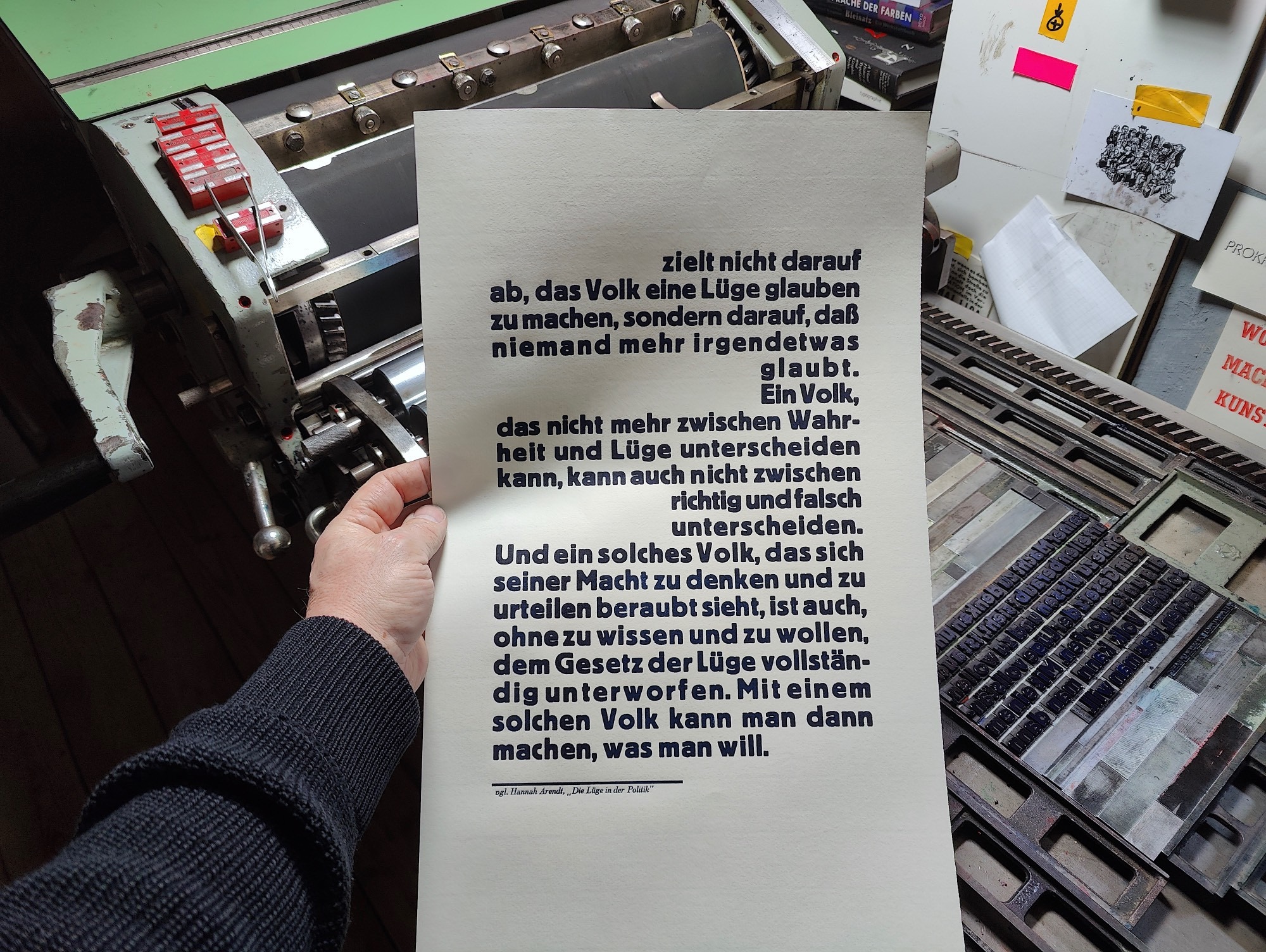 Foto Hand hält die Druckfahne zur Anmutung für die Betrachter*innen vor die Druckmaschine