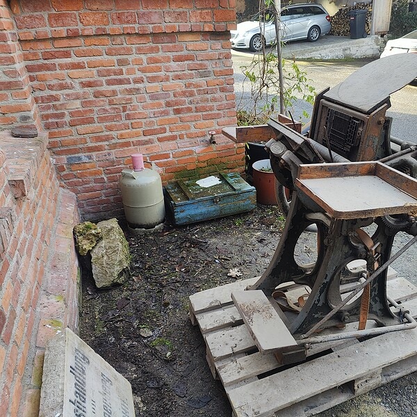 Alte, verrostete Schreibmaschine auf Holzpalette vor Backsteinmauer.