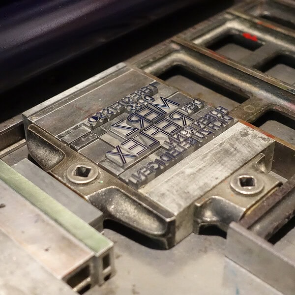 Metallplatte mit eingraviertem Text und Schrauben, industrielle Umgebung.
