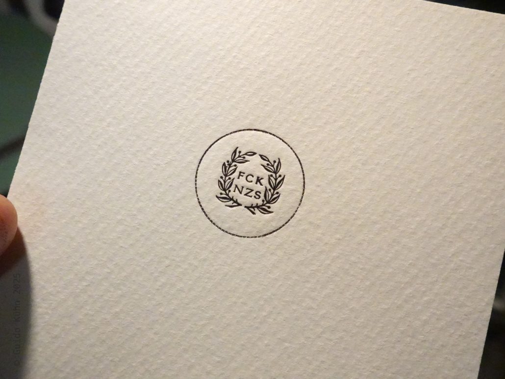 Kleines, rundes Logo mit Laubkranz und den Buchstaben FCK NZS in der Mitte.
