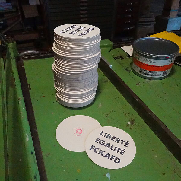 Stapel von weißen Aufklebern mit französischen Slogans auf einem grünen Tisch.