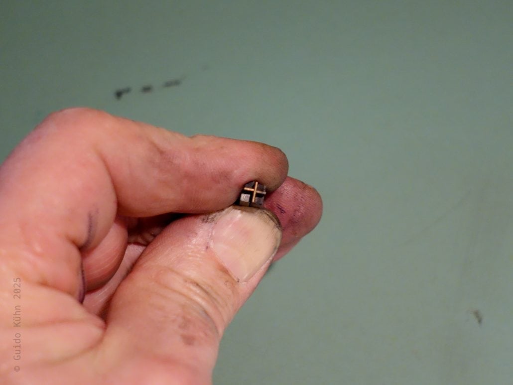 Nahaufnahme eines Fingers mit einem kleinen Metallstück gegen eine grüne Wand.