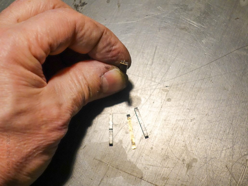 Kleine elektronische Bauteile in einer Hand auf metallischer Oberfläche.