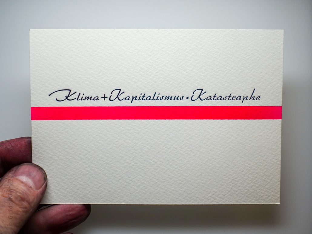 Hand hält Karte mit den Worten Klima + Kapitalismus + Katastrophe.