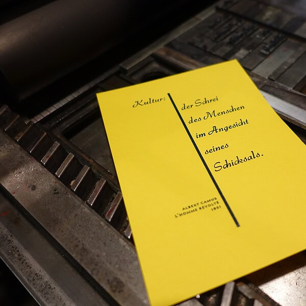 Gelber Flyer mit Zitat über Kultur und Menschen im Anblick des Schicksals.