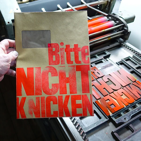 Foto mit C4 Umschlag, der blockartig mit dem Text BITTE NICHT KNICKEN bedruckt ist