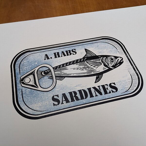 Foto des fertigen Drucks. Das Motiv ist ein zweifarbiger Holzschnitt einer Sardinendose, auf der eine Sardine über und unter der der Schriftzug A. HABS SARDINEN zu lesen ist.