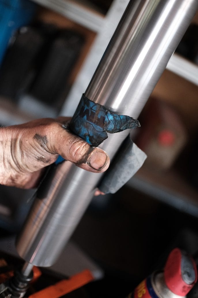 Hand hält eine Metallstange mit Klebeband in einer Werkstatt.