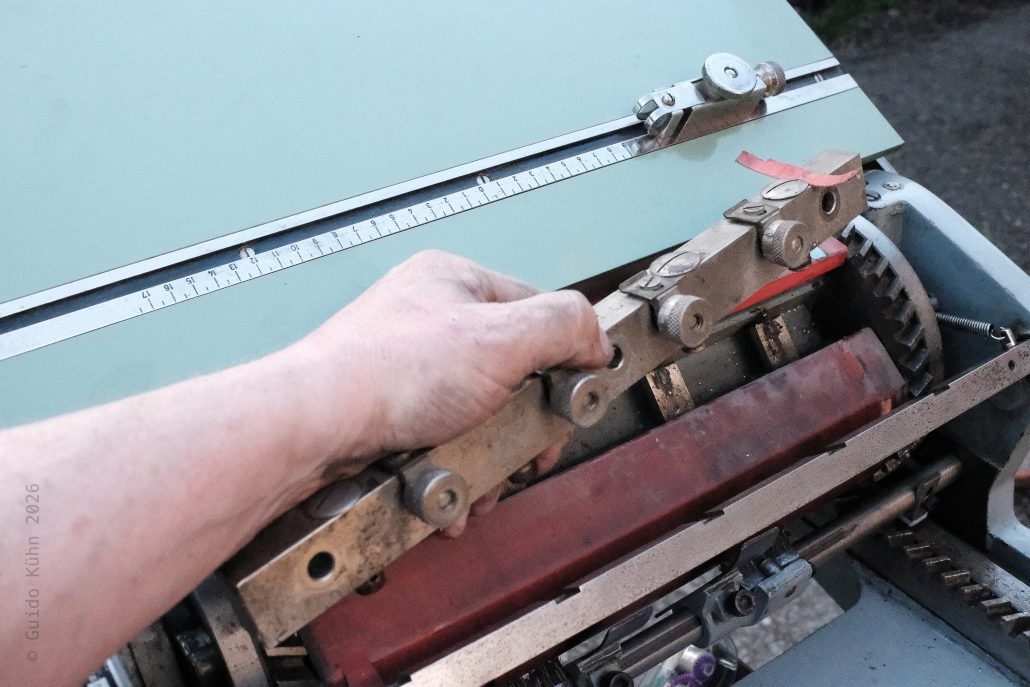 Hand bedient eine alte Druckmaschine in einer Werkstatt.